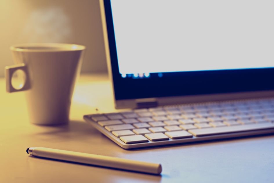 Hands with a pen on a desk with coffee and keyboard