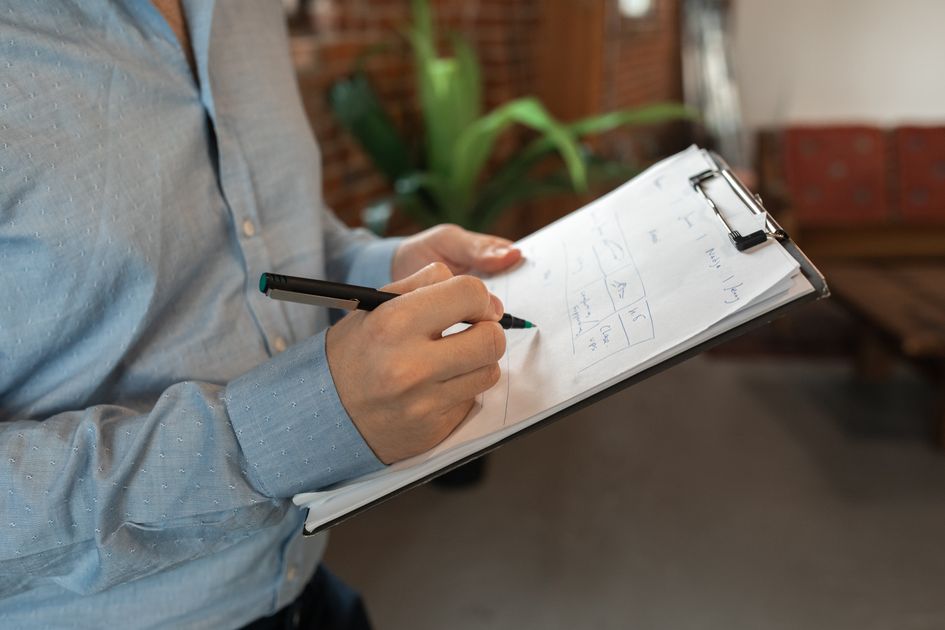 A person writing with a pen on a clipboard indoors