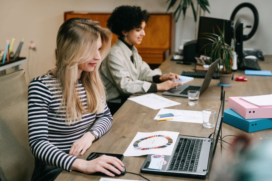 Two colleagues collaborating on laptops in a modern office