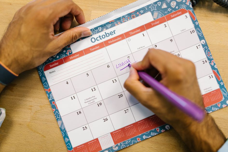 A person writing a reminder on a calendar with a purple pen