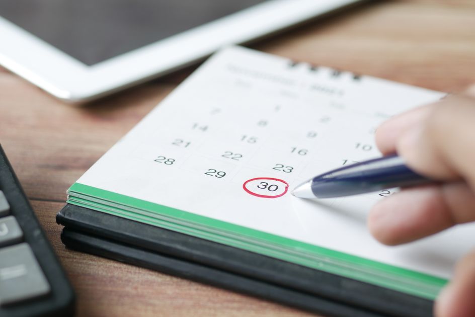 A hand marking a date on a calendar with a pen