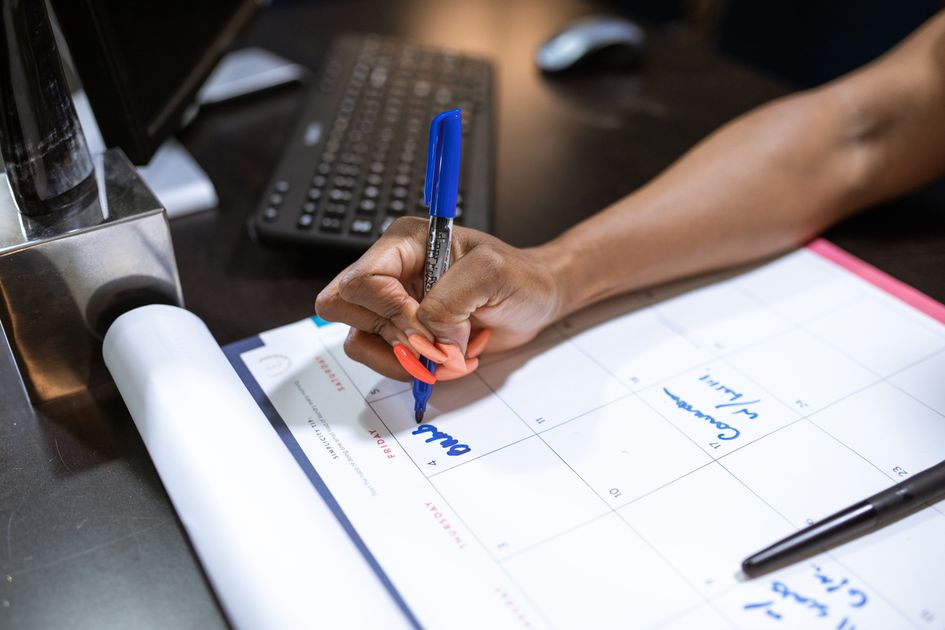 A hand writing notes on a calendar with a blue marker