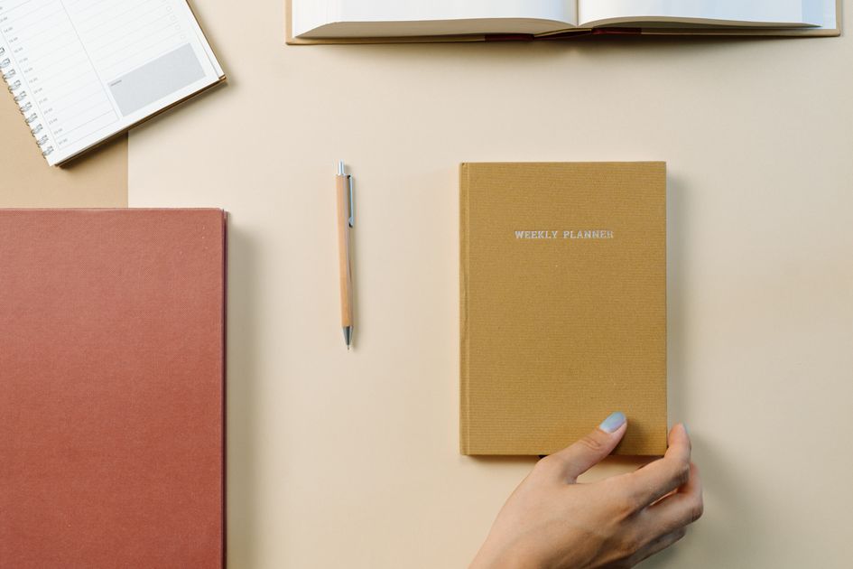 A weekly planner, notebook, and pen on a desk