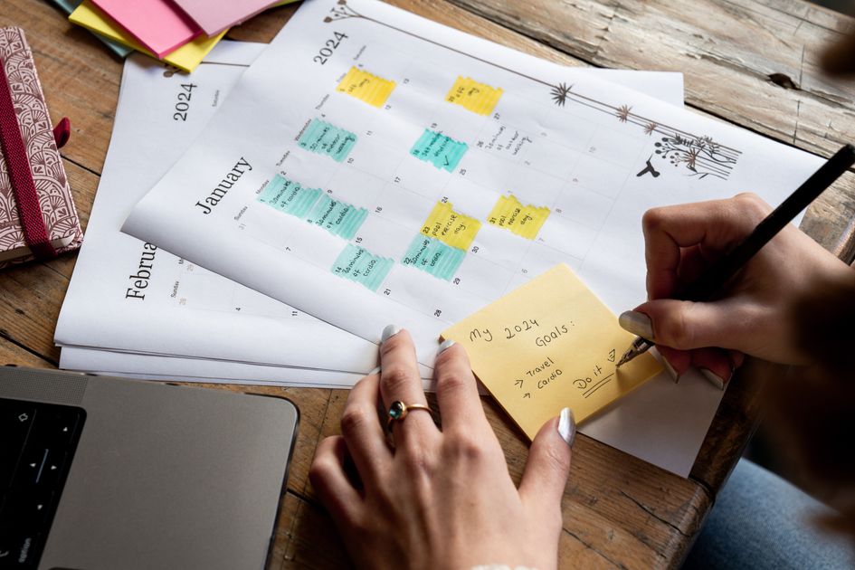 A person writing content plans on a sticky note beside a calendar