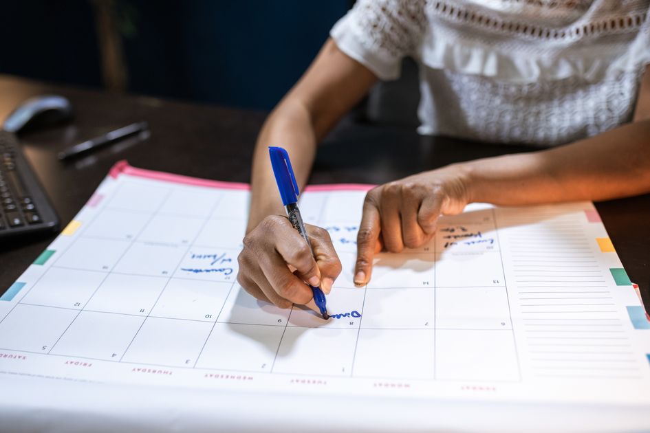 A person writing important notes on a desk calendar in an office