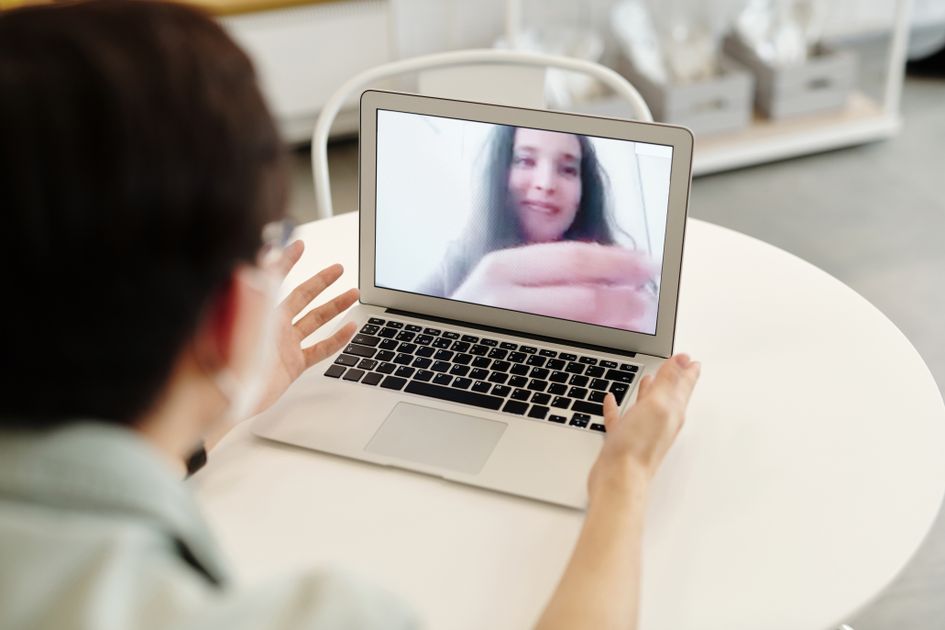 A woman waving during a video call with earpods in