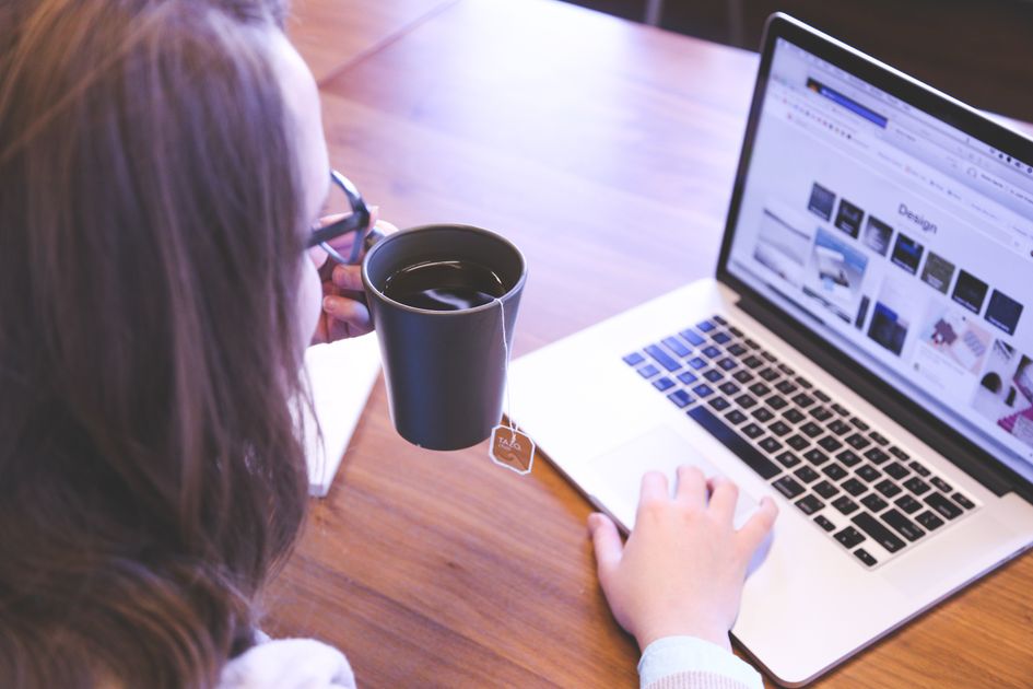 A person enjoying coffee while working on a laptop at a home desk