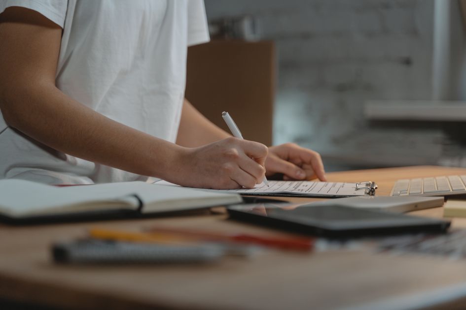 A person writing on a clipboard at a desk with office supplies