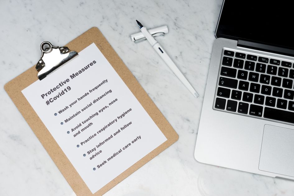 A pen resting between a clipboard and laptop on a marble surface
