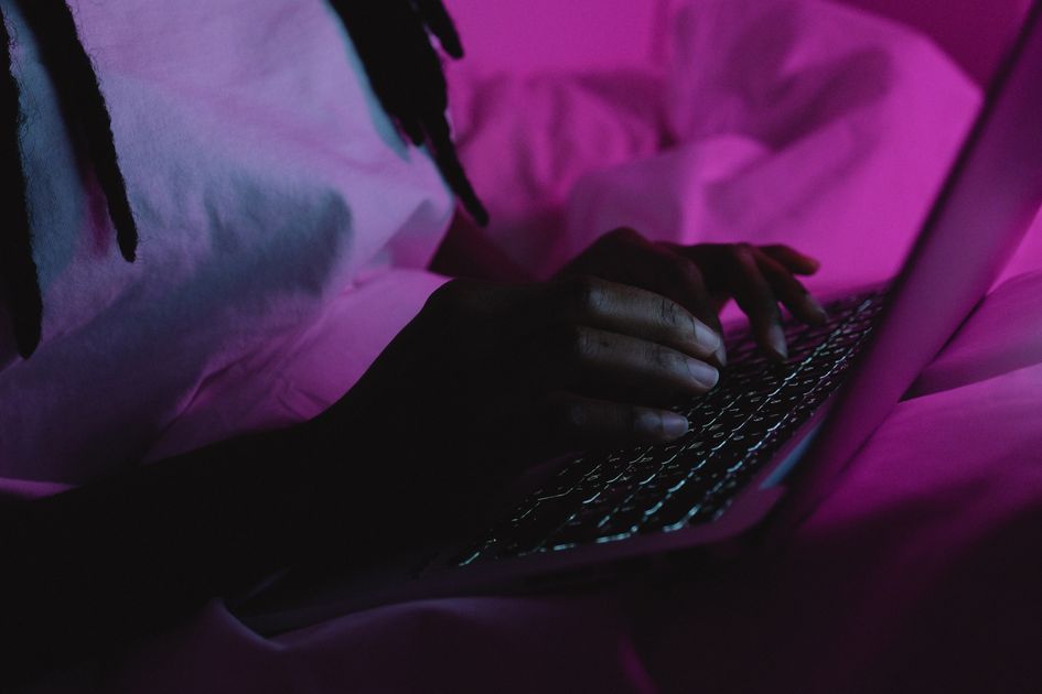 A person typing on a laptop under vibrant evening lighting
