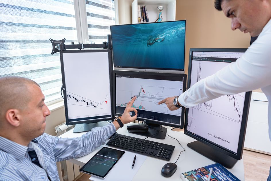 Two professionals analyzing data on multiple computer screens in an office