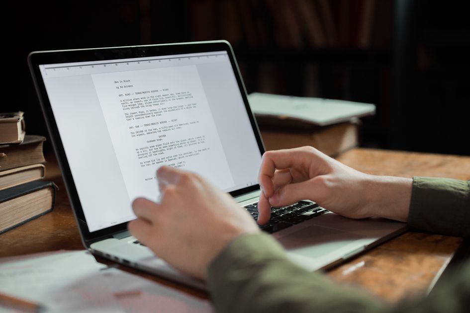 A person typing on a laptop in a cozy workspace with books around