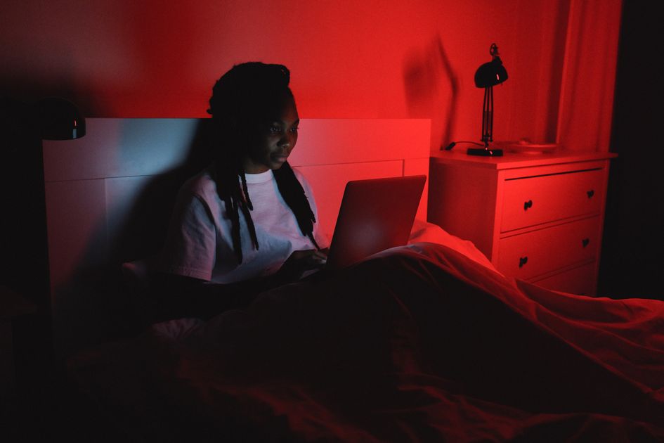 A woman sitting in bed using a laptop under ambient light
