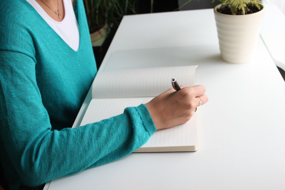 A person writing in a notebook at a tidy desk