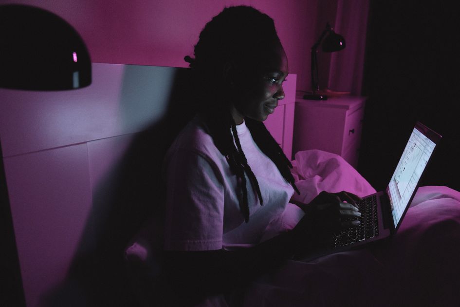 A woman using a laptop in bed under soft lighting