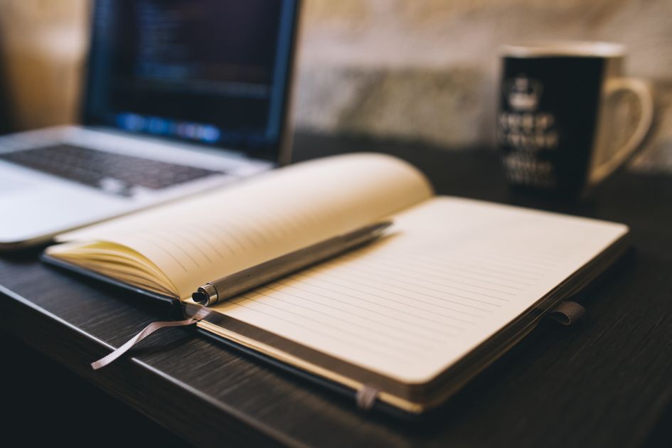 An open notebook and pen beside a laptop