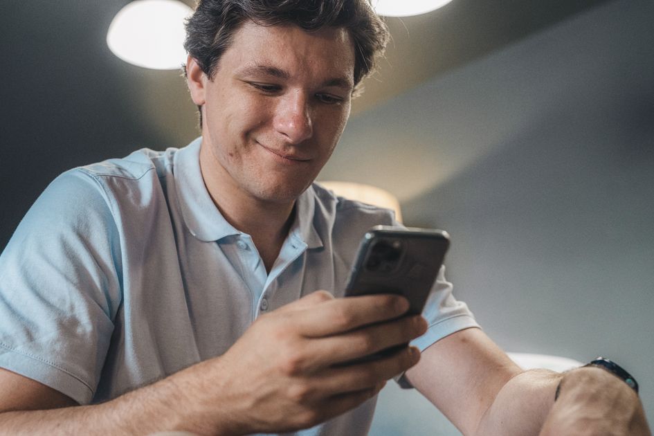 A man in a blue polo shirt smiling while using a smartphone