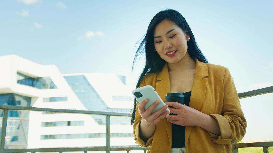 A woman texting on her smartphone while holding coffee outdoors