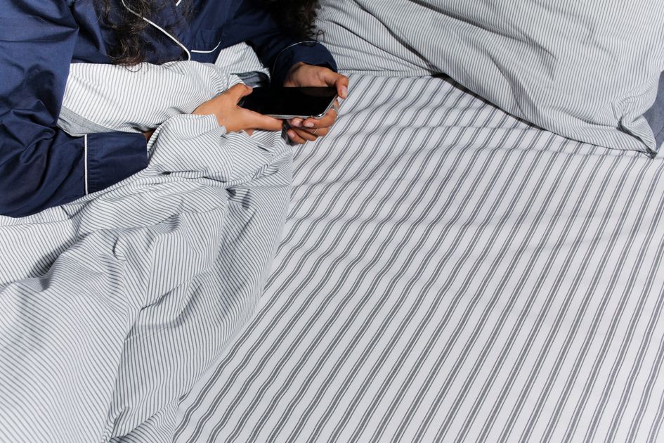 A person in pajamas using a smartphone in bed
