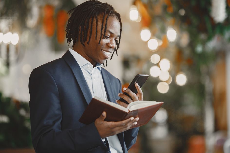 A smiling businessman multitasking with a book and smartphone