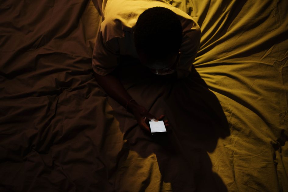 An overhead shot of a person using a smartphone on a bed