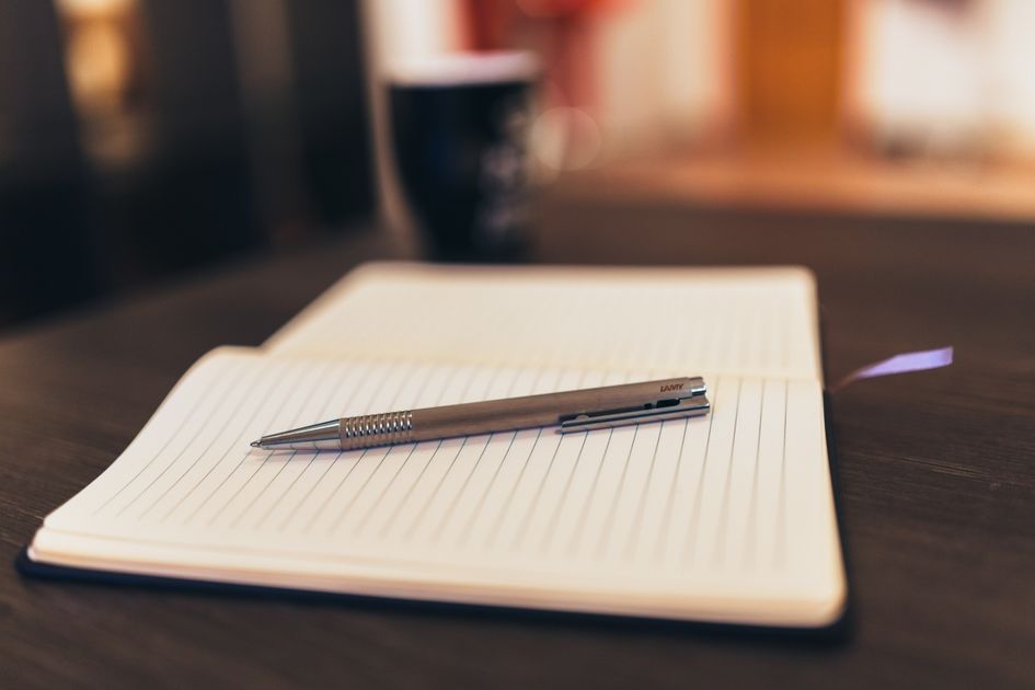 An open notebook and pen next to a mug on a desk