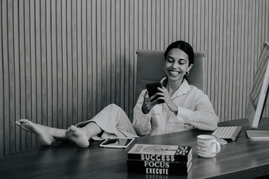 A woman relaxing at her desk with feet up, smiling at her phone