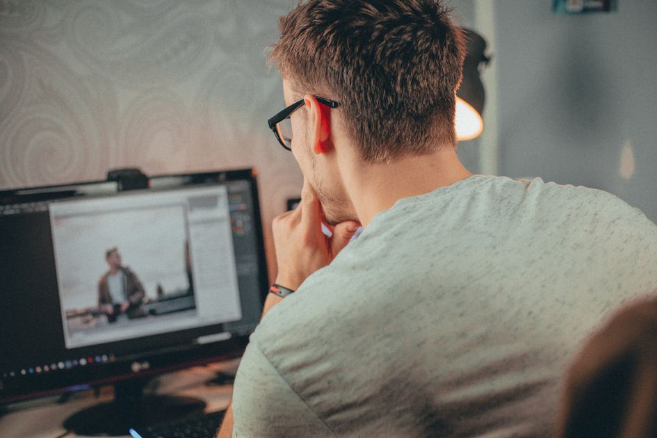 A man in glasses focused on editing a photo on his desktop computer
