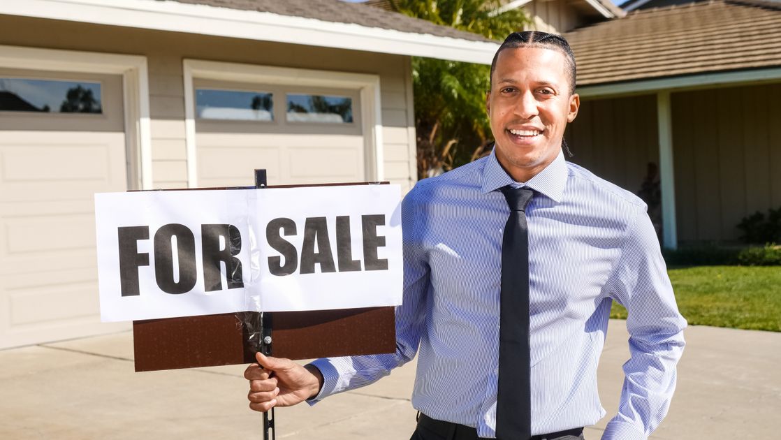 A real estate agent holding a for-sale sign outside a house