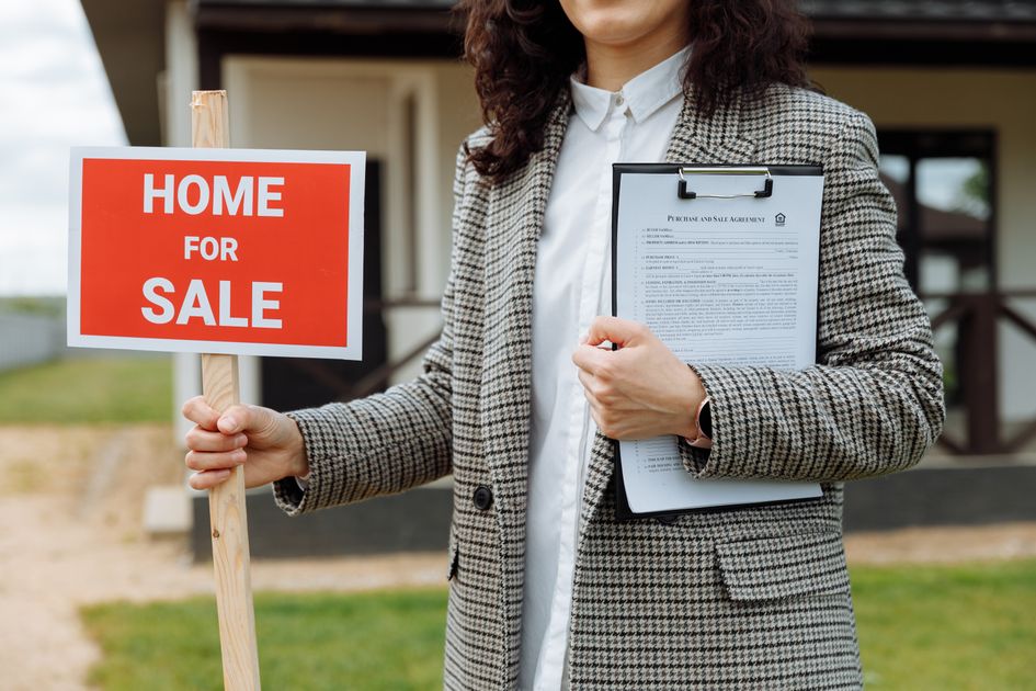 A real estate agent holding a clipboard and for-sale sign
