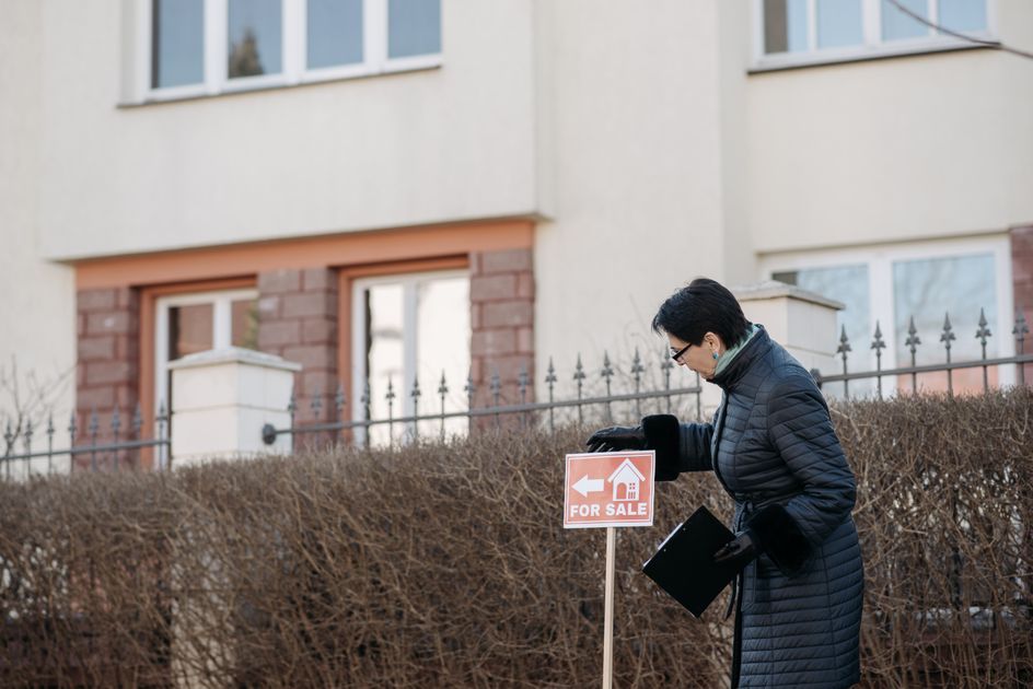 A real estate agent standing beside a for-sale sign