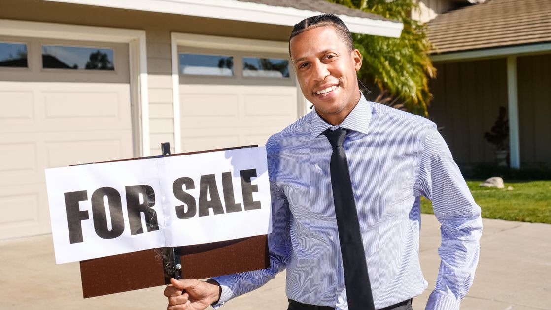 A real estate agent with a for-sale sign on a sunny day