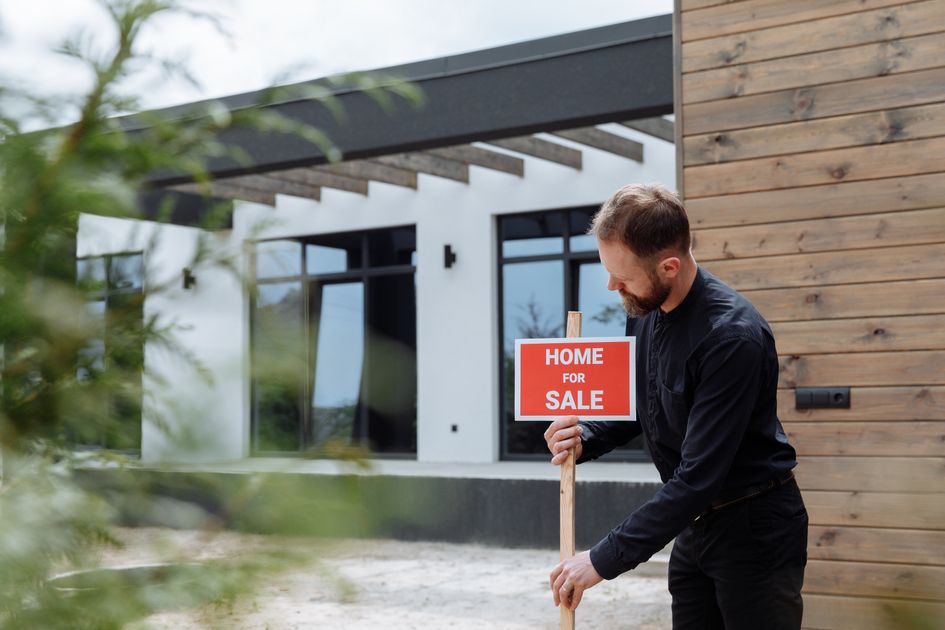 An agent placing a home for-sale sign outside a modern house