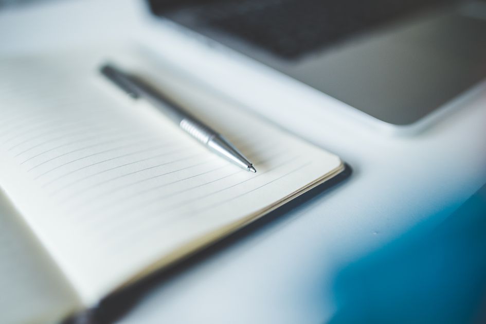 A notebook and pen beside a laptop in a tidy workspace