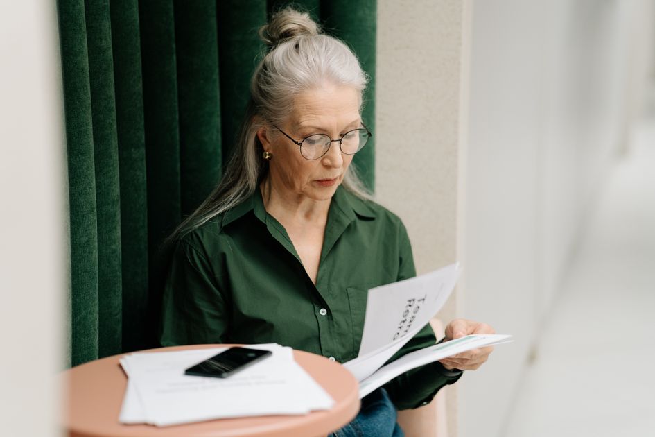 A woman reading papers at a small table, focused and thoughtful