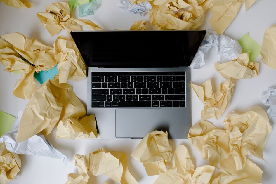A laptop surrounded by scattered papers on a busy desk