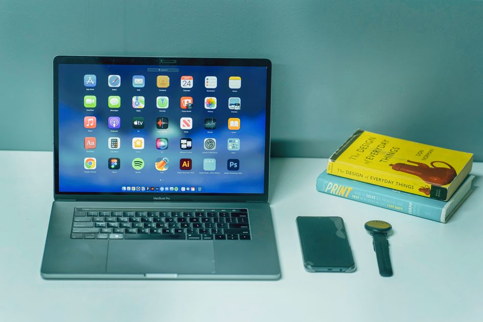 A desk setup featuring a laptop, smartphone, and watch