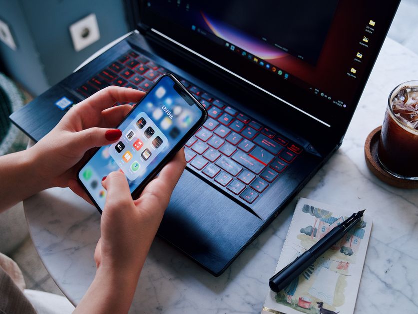 Hands holding a smartphone over a laptop