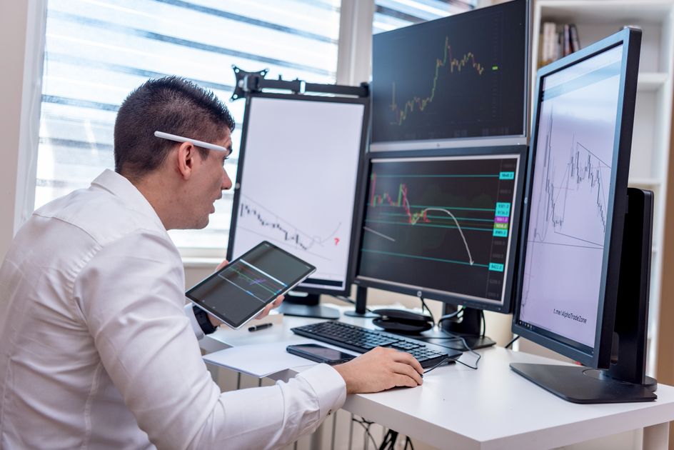 A man analyzing graphs on multiple screens at a workstation