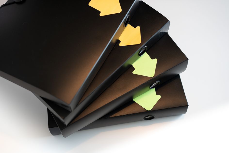 A stack of black ring binders with colored labels