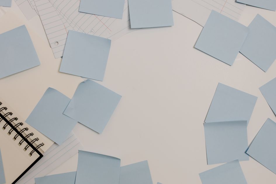 A desk with sticky notes, a spiral notepad, and lined papers