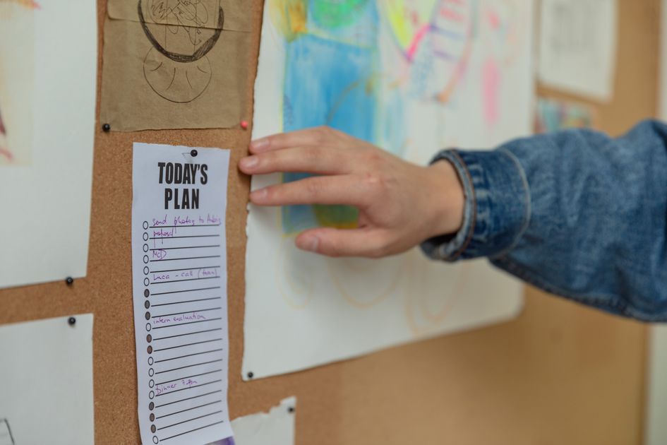 A hand pinning a to-do list on a corkboard