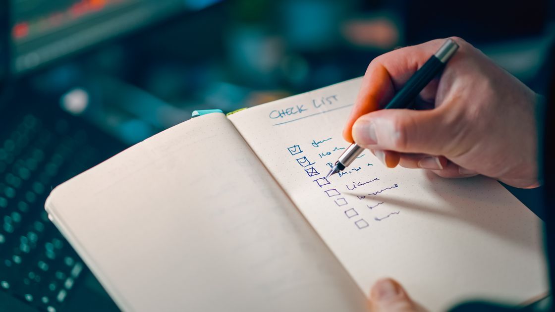 A hand writing in a notebook with a checklist