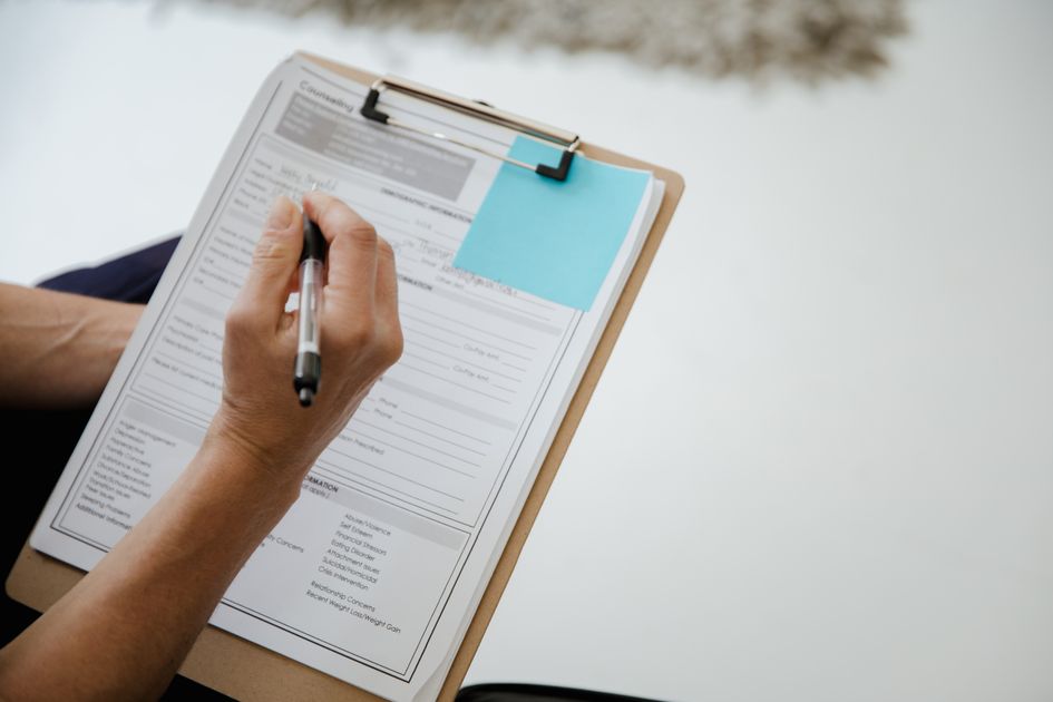 A person writing on a document using a clipboard