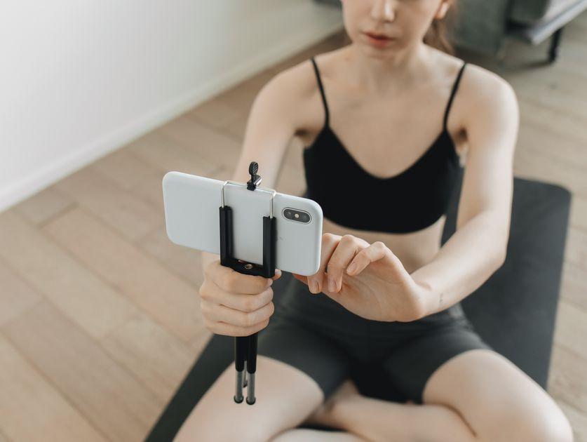 A woman practicing yoga with a smartphone on a tripod nearby