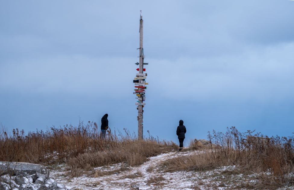 Two people in winter clothing exploring a snowy landscape near a directional signpost