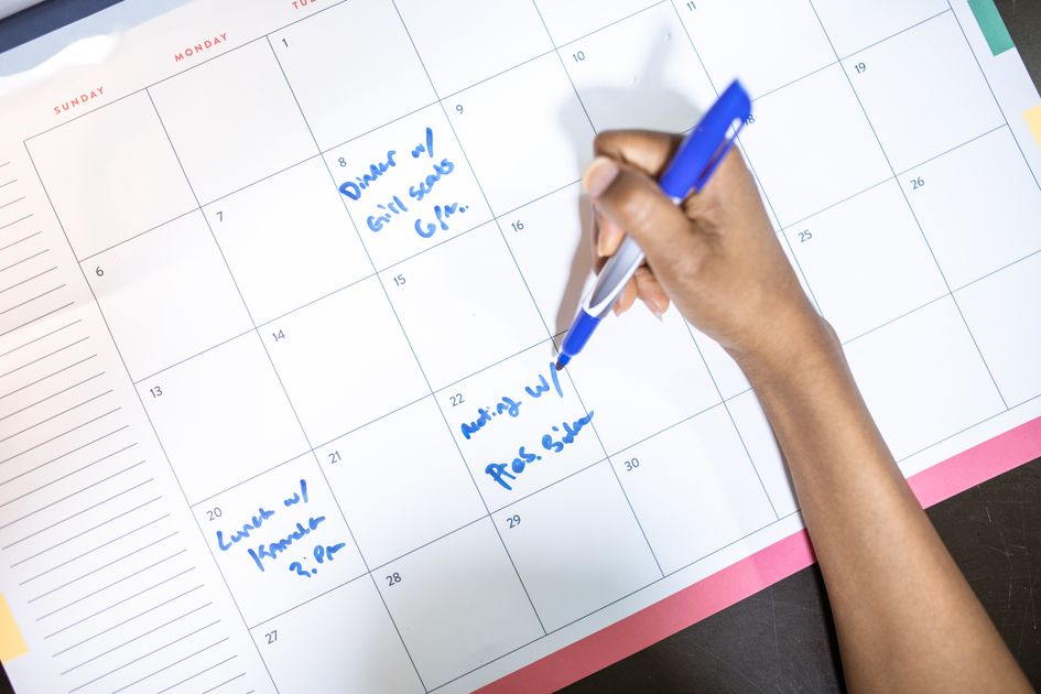 A person writing appointments on a calendar with a blue pen