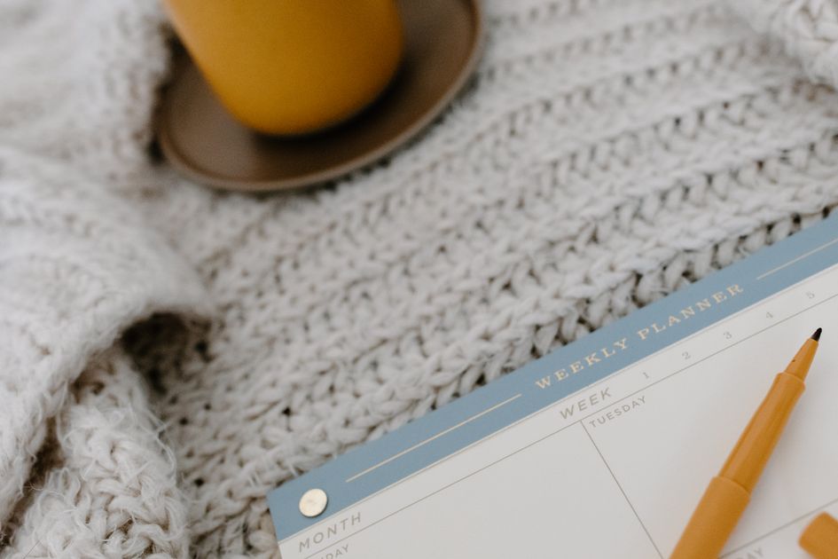 A cozy flat lay with a weekly planner, pen, and warm drink