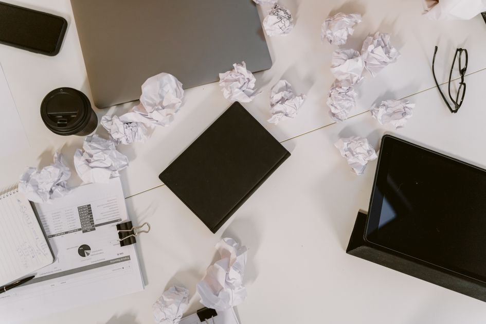 A cluttered desk with papers piled beside a laptop