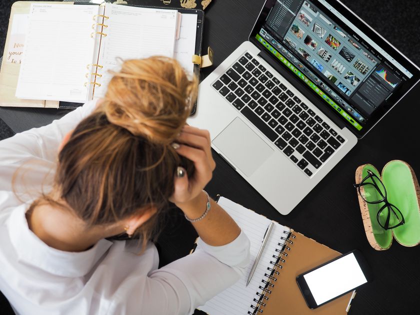An overhead view of a stressed woman working at a desk with a laptop and phone